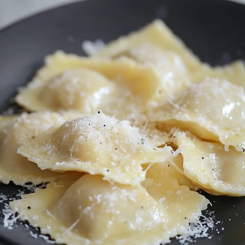 Une assiette de pâtes garnie de fromage et de poivre noir.