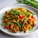 Sur un plateau, un plat généreux de riz, boeuf et tomates avec des haricots verts.