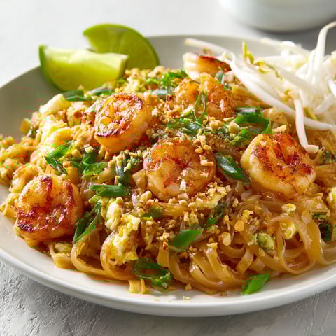 Sur une table, une assiette de pad thaï crevettes pleine de légumes frais et noix de coco attend d’être dégustée.
