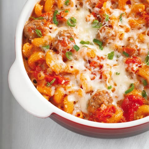 On vient de servir une belle portion de macaronis aux tomates et saucisses italiennes dans un grand contenant en verre.