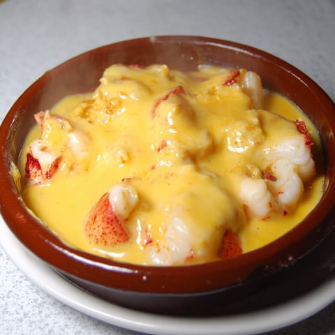 Un bol en terre rempli de homard et saint-jacques nappés de crème chaude.