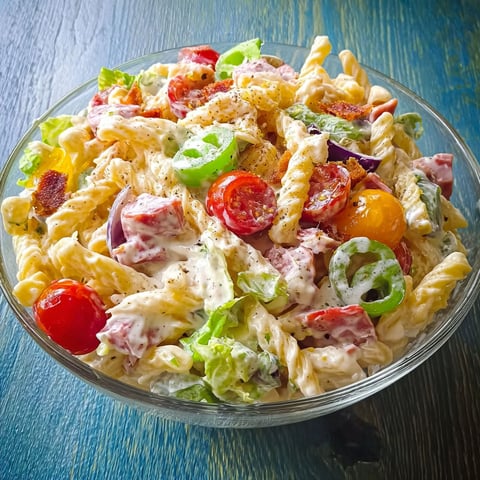 Un grand bol rempli de couches : tomates, concombres, salade verte, pâtes. Le tout posé sur une jolie table.