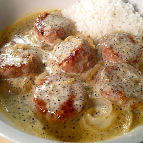 Un bol plein de paupiettes de porc nappées de crème fraîche est posé sur la table.