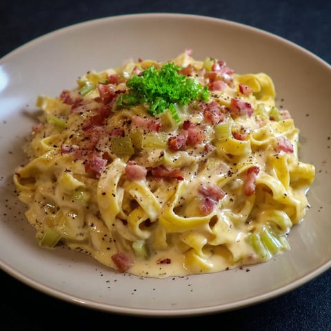 Assiette de tagliatelles à la carbonara aux poireaux posée sur une planche.
