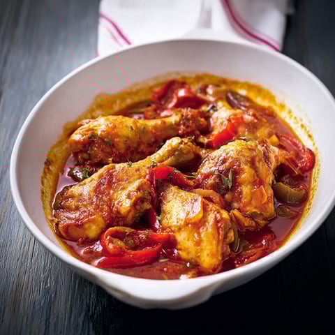 Un bon poulet basquaise plein de tomates, poivrons et oignons sur une table conviviale.